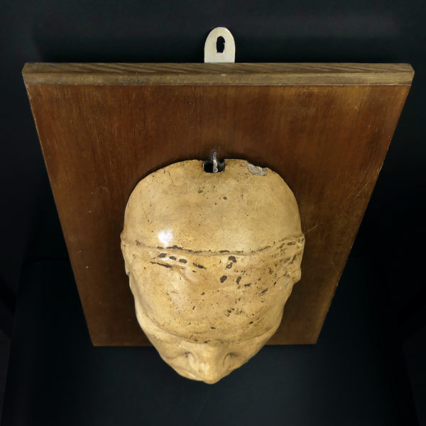 Masque mortuaire ancien en plâtre présenté sur planche de bois Mi-XXe (dessus)